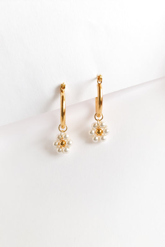 A close-up of a pair of gold hoop earrings with flowers made of small white pearls with a gold bead center.